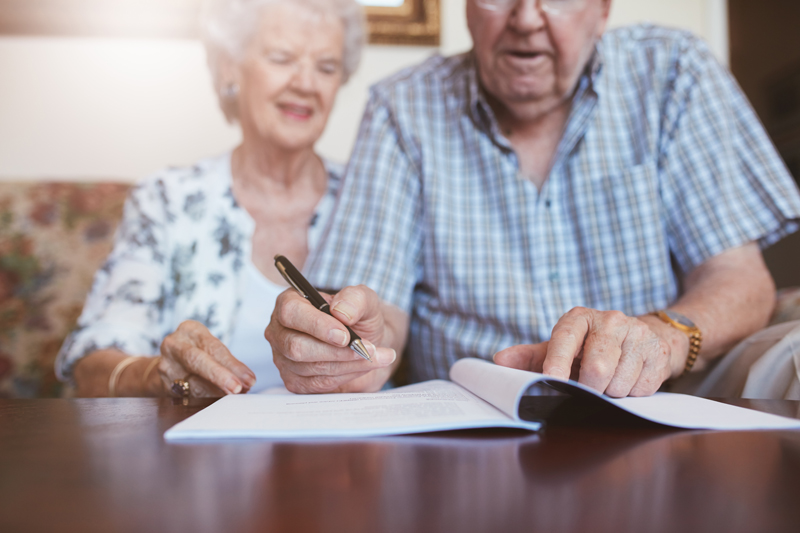 image shows senior citizen couple seated and man is signing his living will prepared by The Pearce Law Group in Myrtle Beach SC